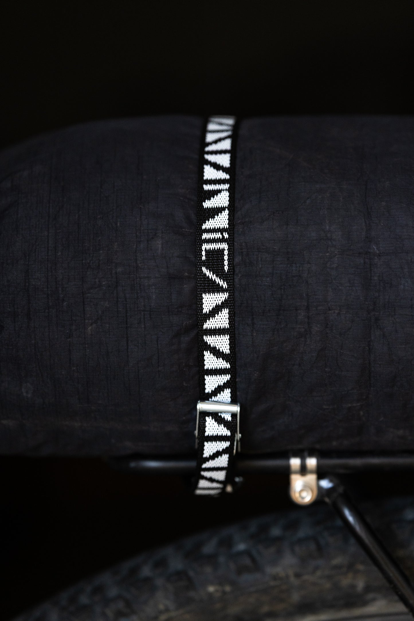 Black bicycle rack bag with a patterned cam strap on a dark background