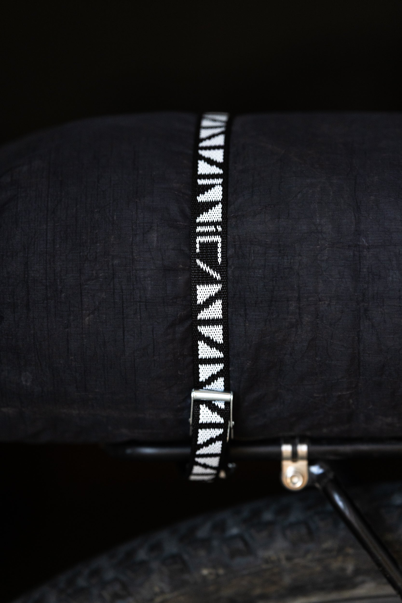 Black bicycle rack bag with a patterned cam strap on a dark background