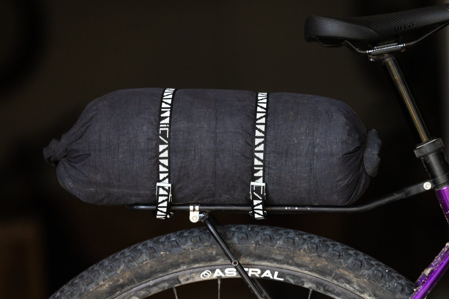 Black bikepacking bag strapped to a bicycle with black and white patterned cam straps.